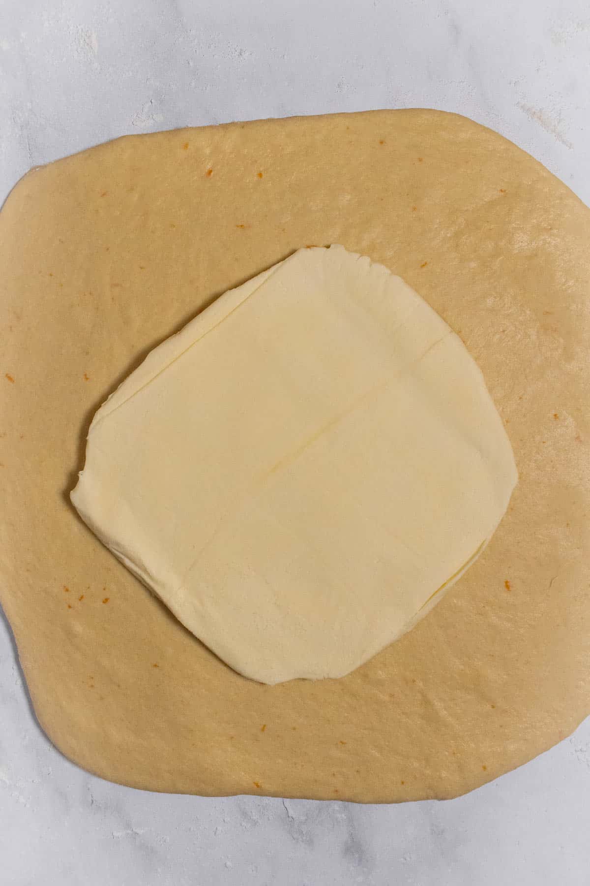 Rolled-out cinnamon roll dough with a butter block on top.