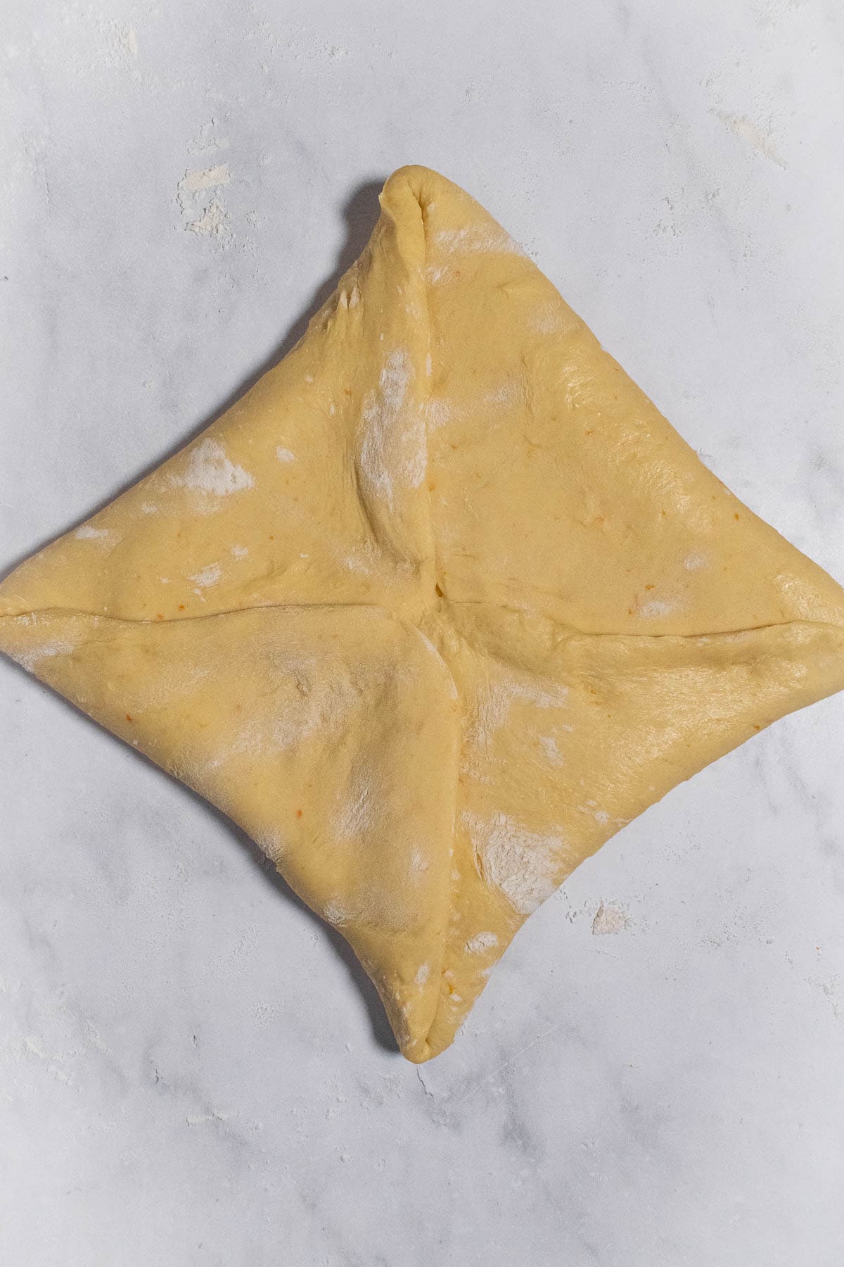 A folded square of enriched orange bread dough.