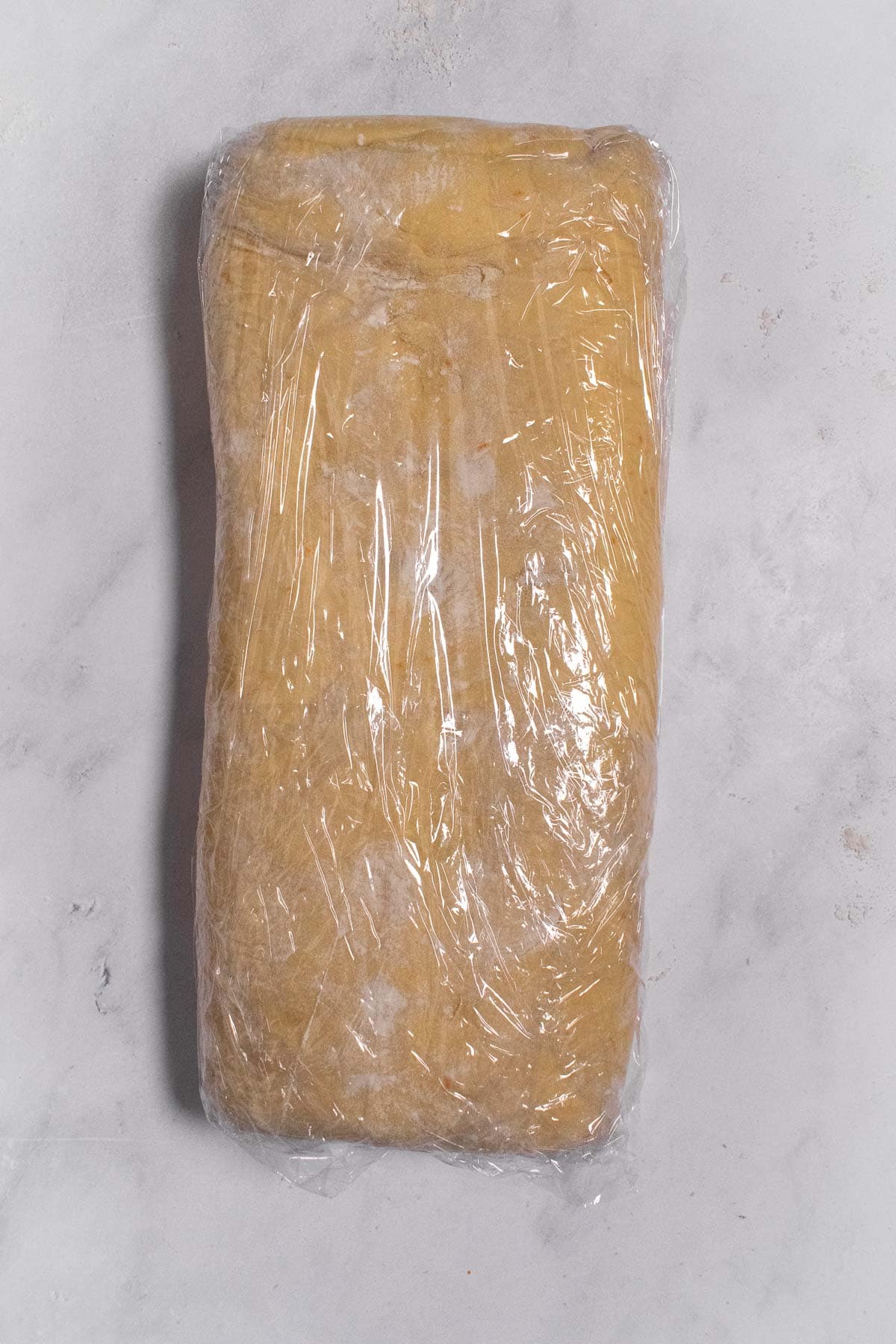 A small rectangle of bread dough wrapped in plastic wrap.