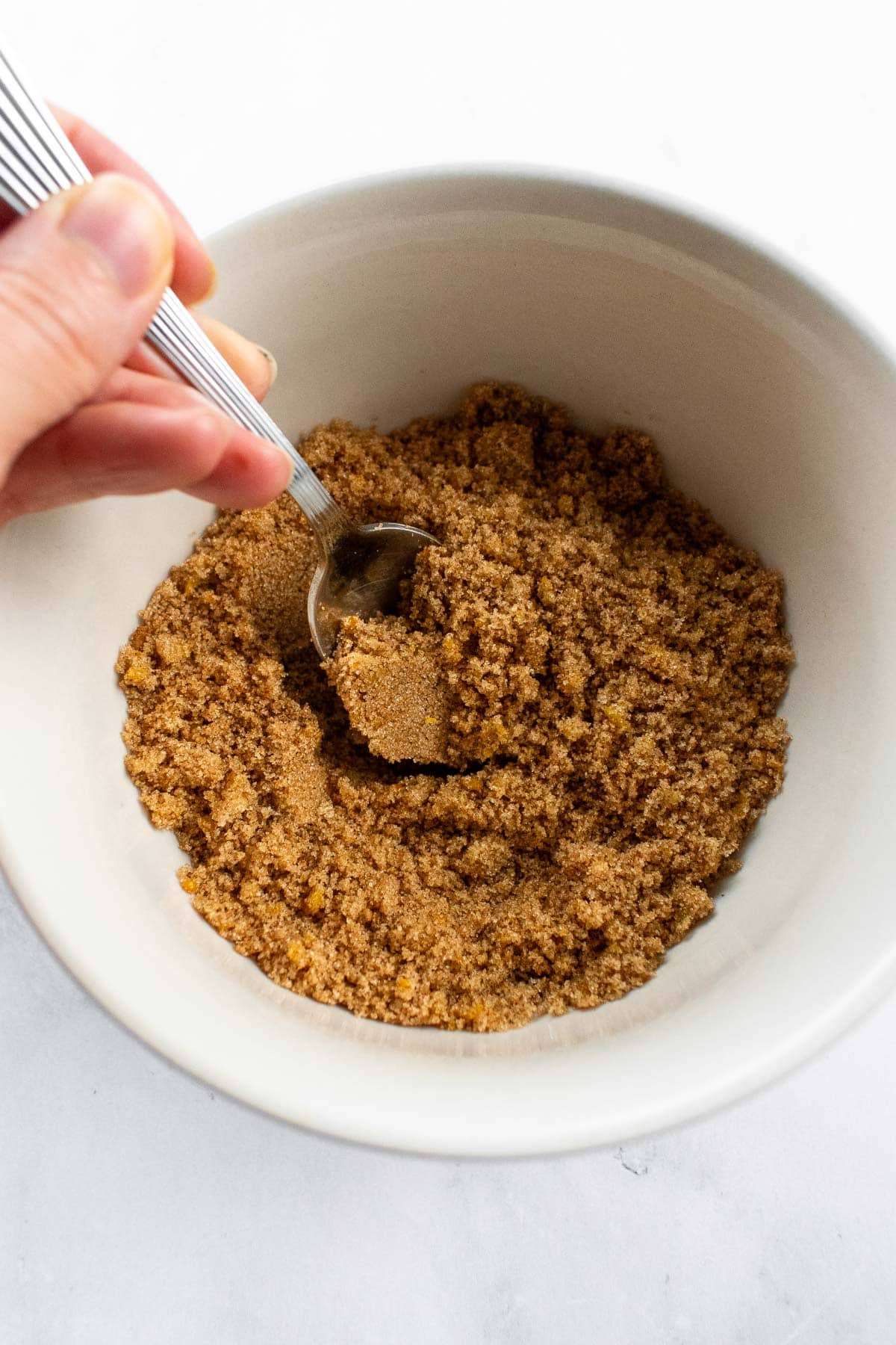 A hand stirring cinnamon sugar in a bowl with a spoon.
