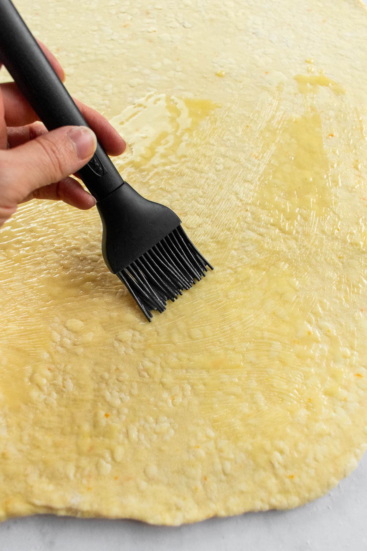 A hand brushing melted butter onto rolled-out bread dough.