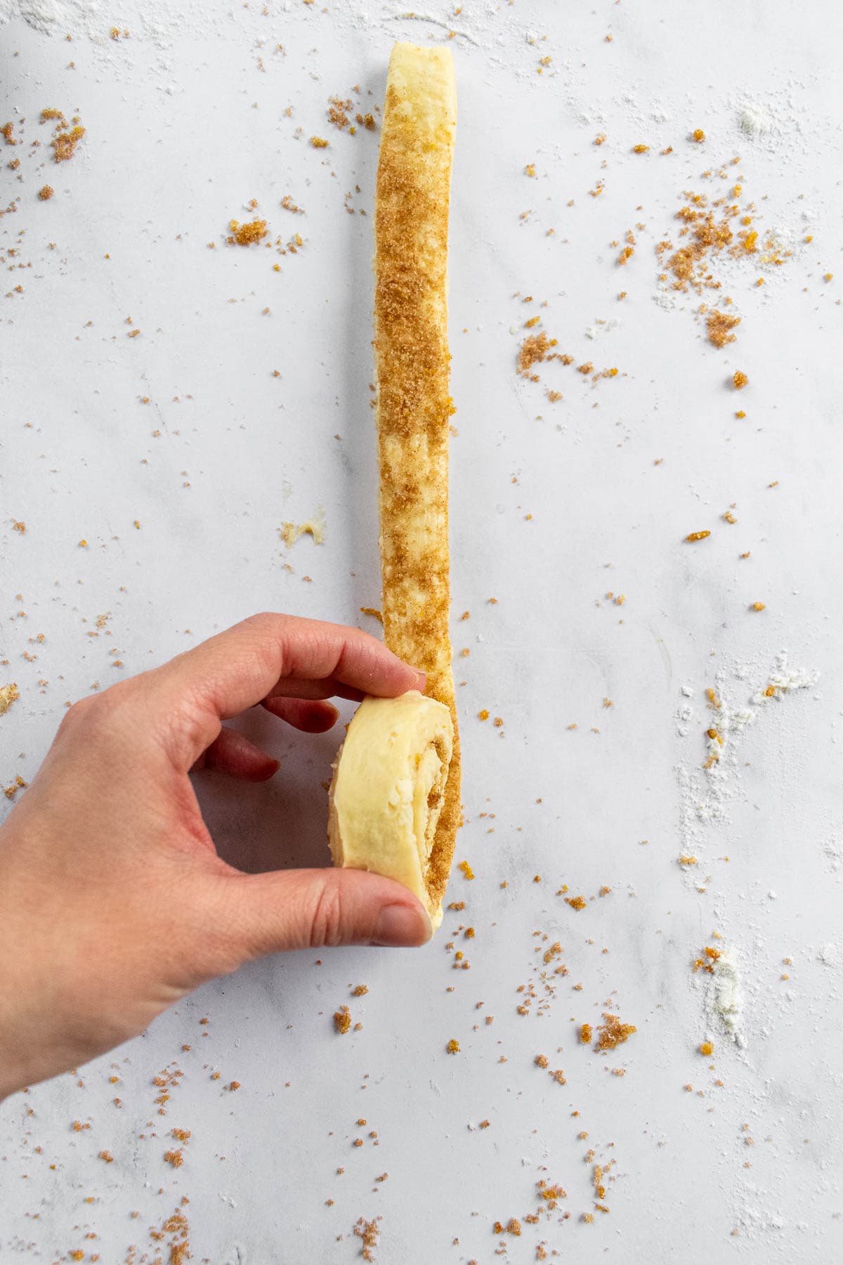 A hand forming a spiral of dough on a marble surface.