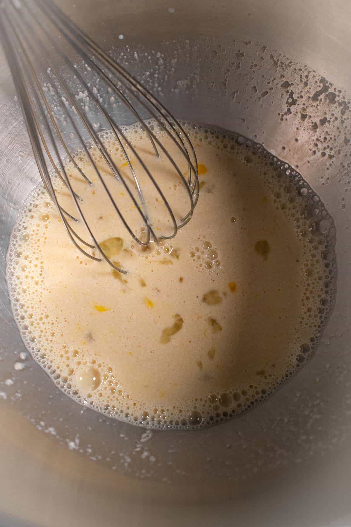 Milk, yeast, sugar, and eggs whisked in a metal bowl.