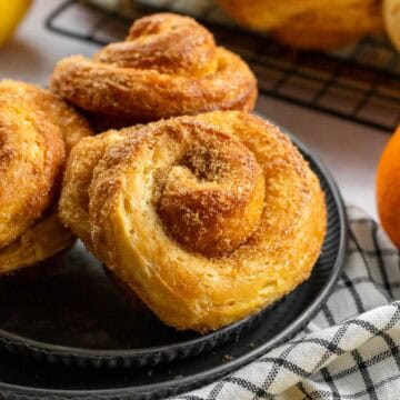 Three morning buns on a metal plate next to more buns on a cooling rack.