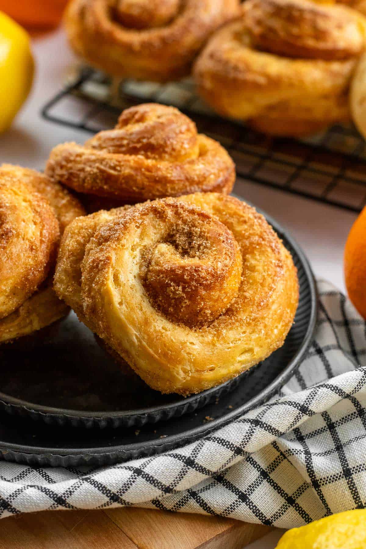 Three morning buns on a metal plate next to more buns on a cooling rack. 