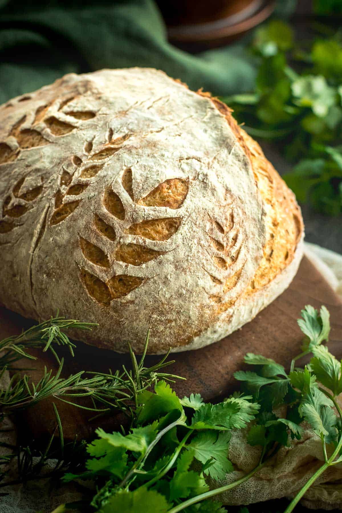 A loaf of crusty bread score with leaf sprigs.