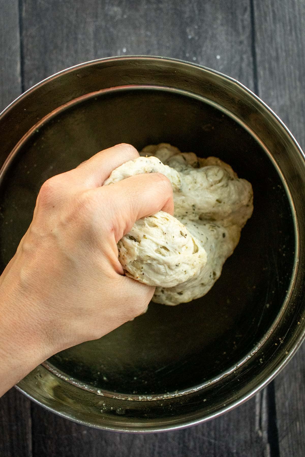 A hand squeezing bread dough above a mixing bowl.