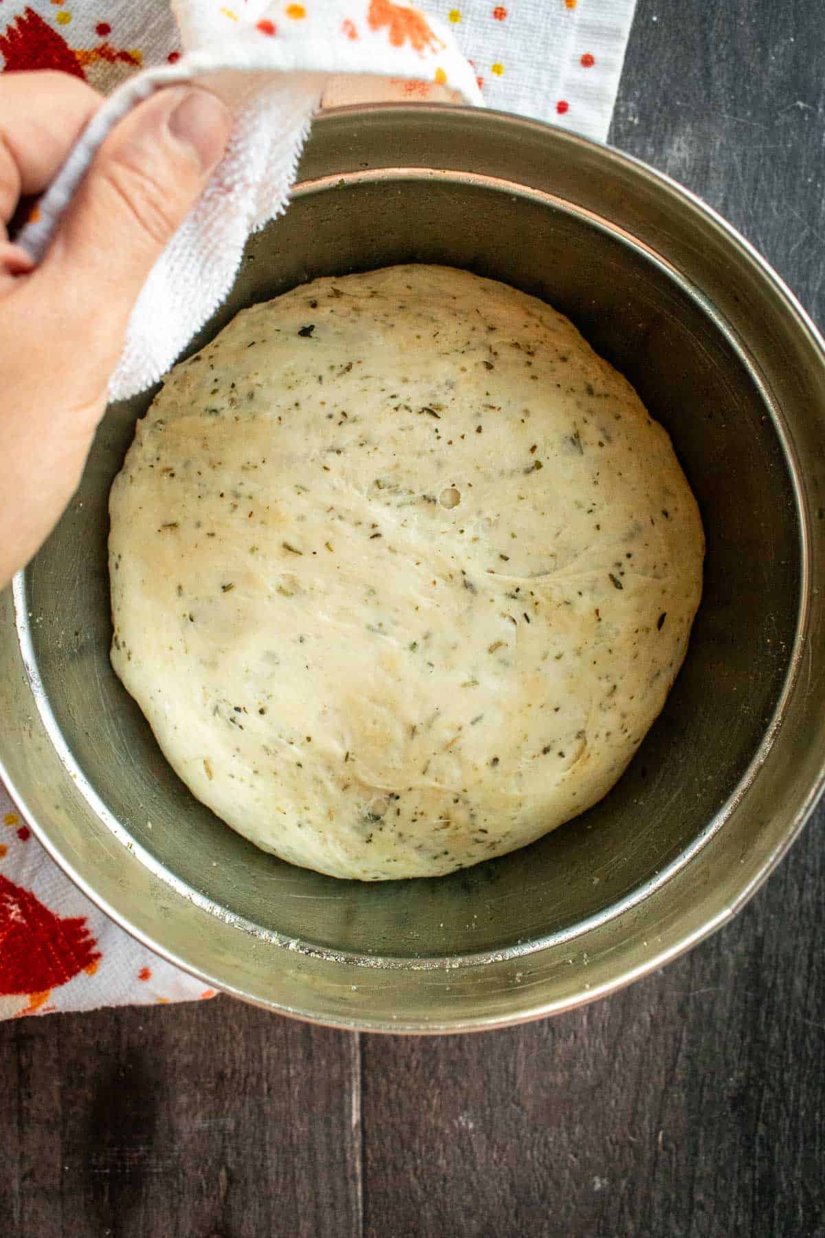 Risen bread dough with herbs in a metal mixing bowl.