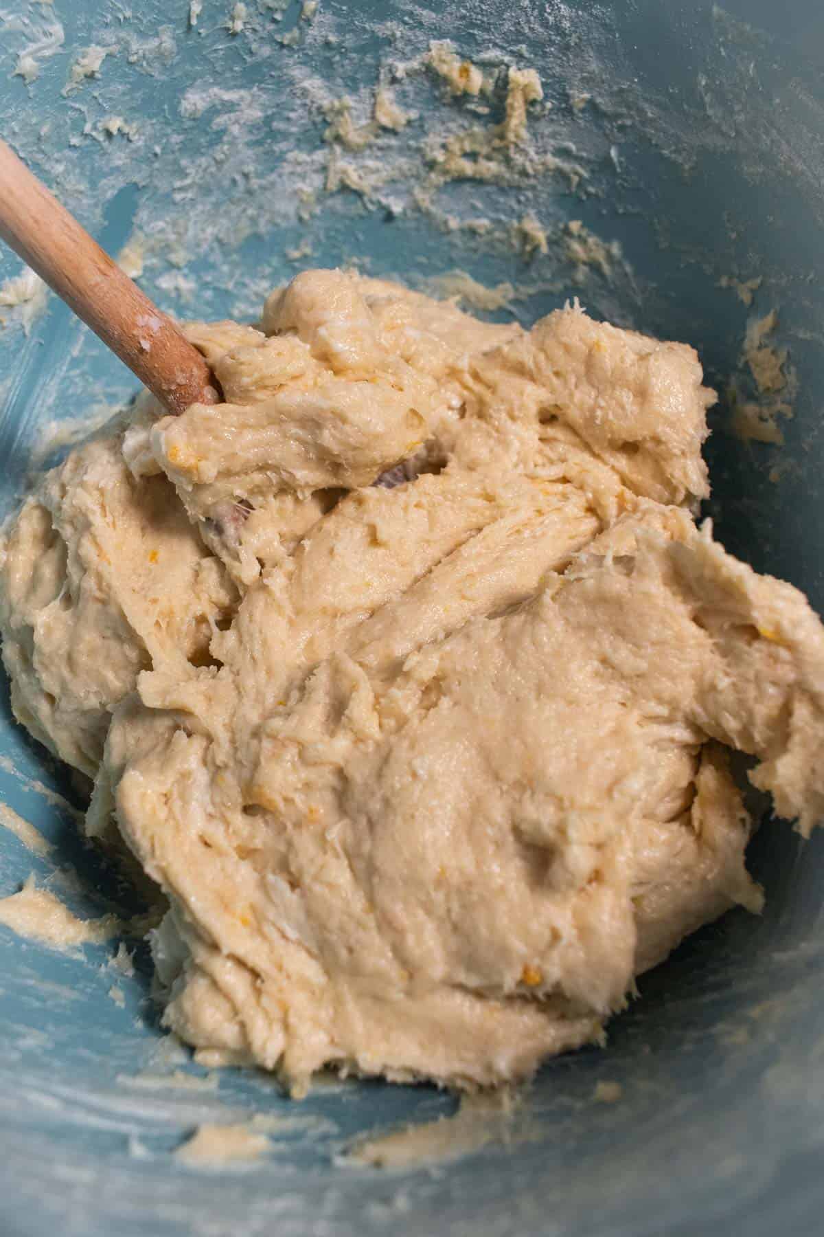 A sticky bread dough in a mixing bowl with a wooden spoon.