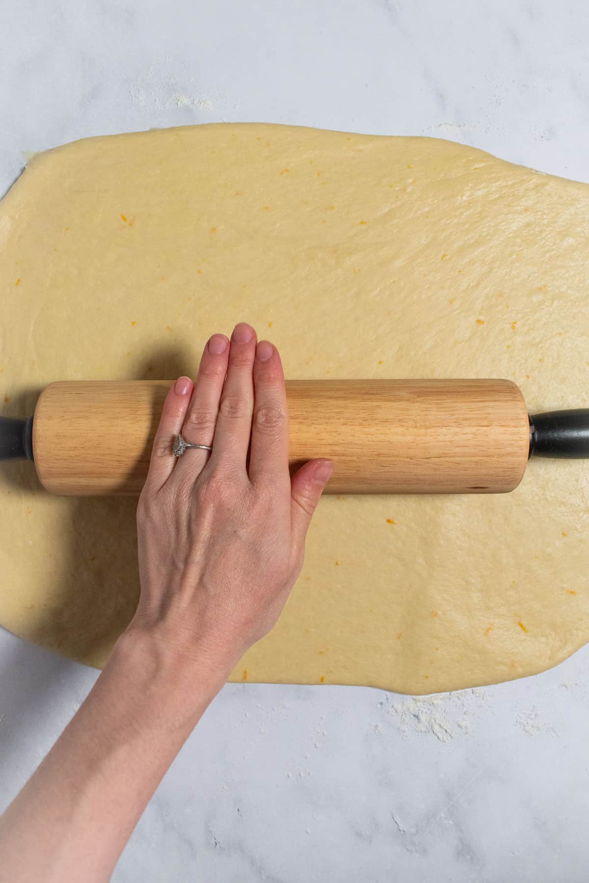 A hand rolling out bread dough with a rolling pin.