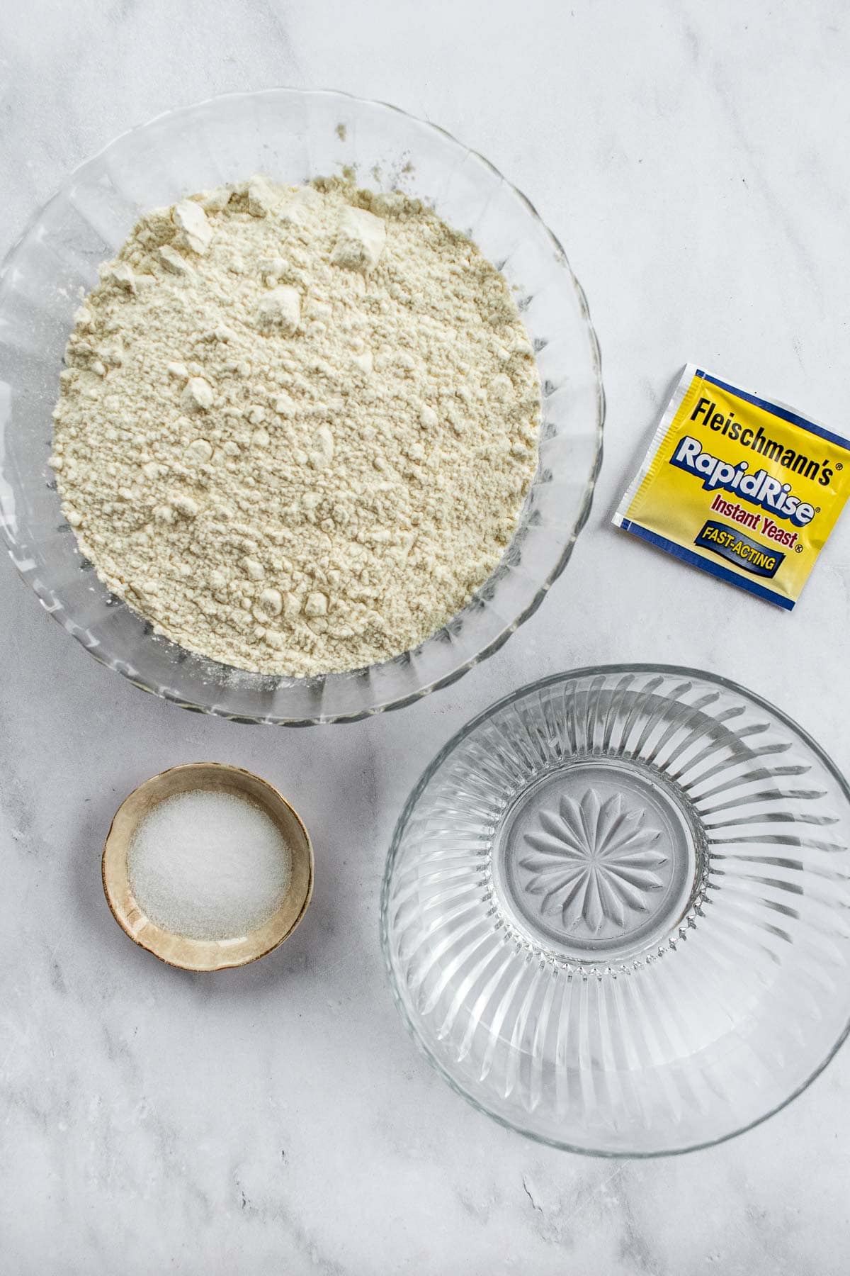 Bowls of flour and water next to a packet of dry yeast and a dish of salt.