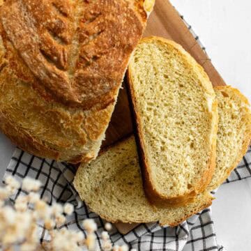 Two slices of white artisan bread on a cutting board next to a baked loaf.