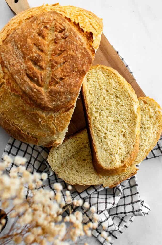 Two slices of white artisan bread on a cutting board next to a baked loaf.