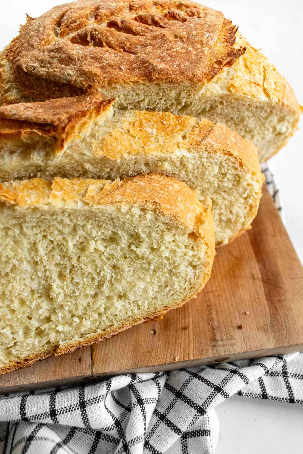 Two slices of white rustic bread leaning against the rest of the loaf on a wood board.