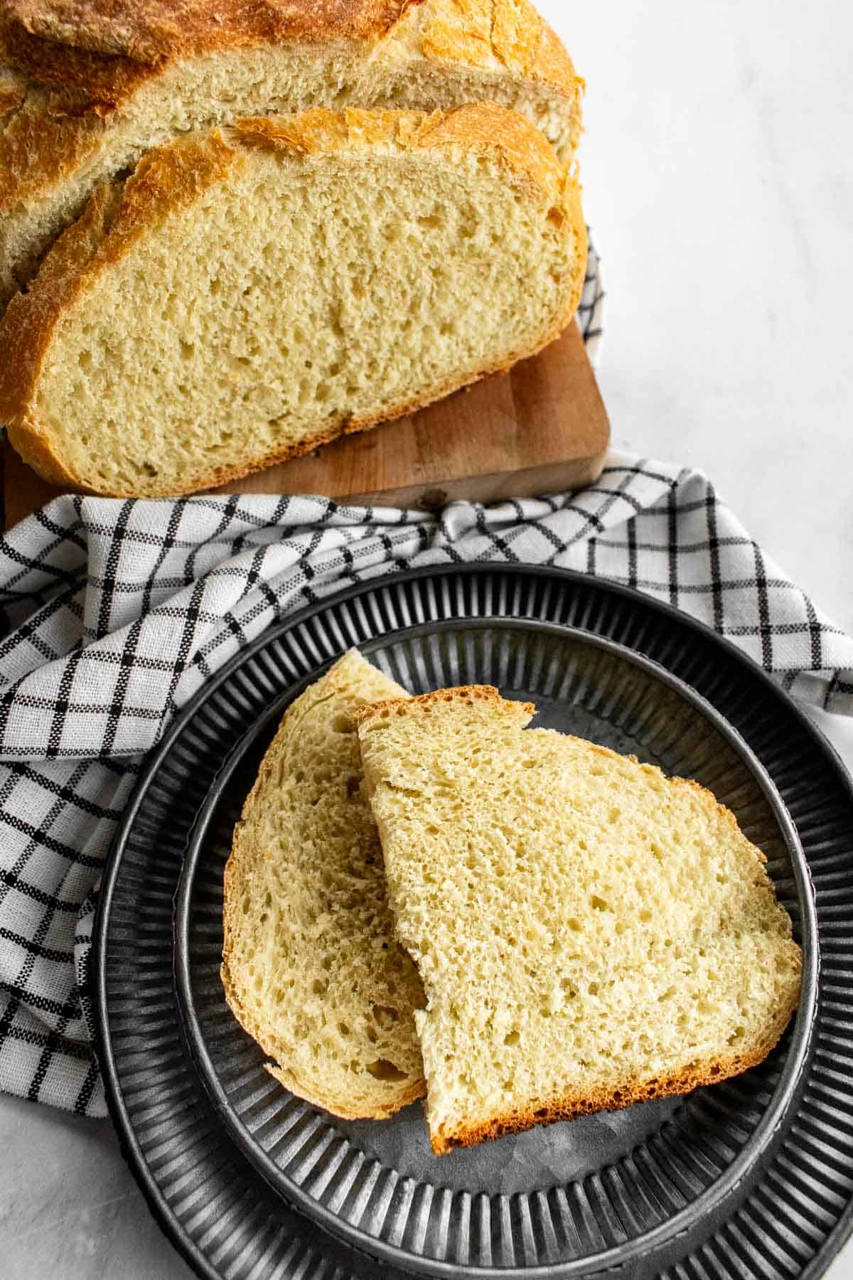 Two slices of white dutch oven bread on stacked metal plates.