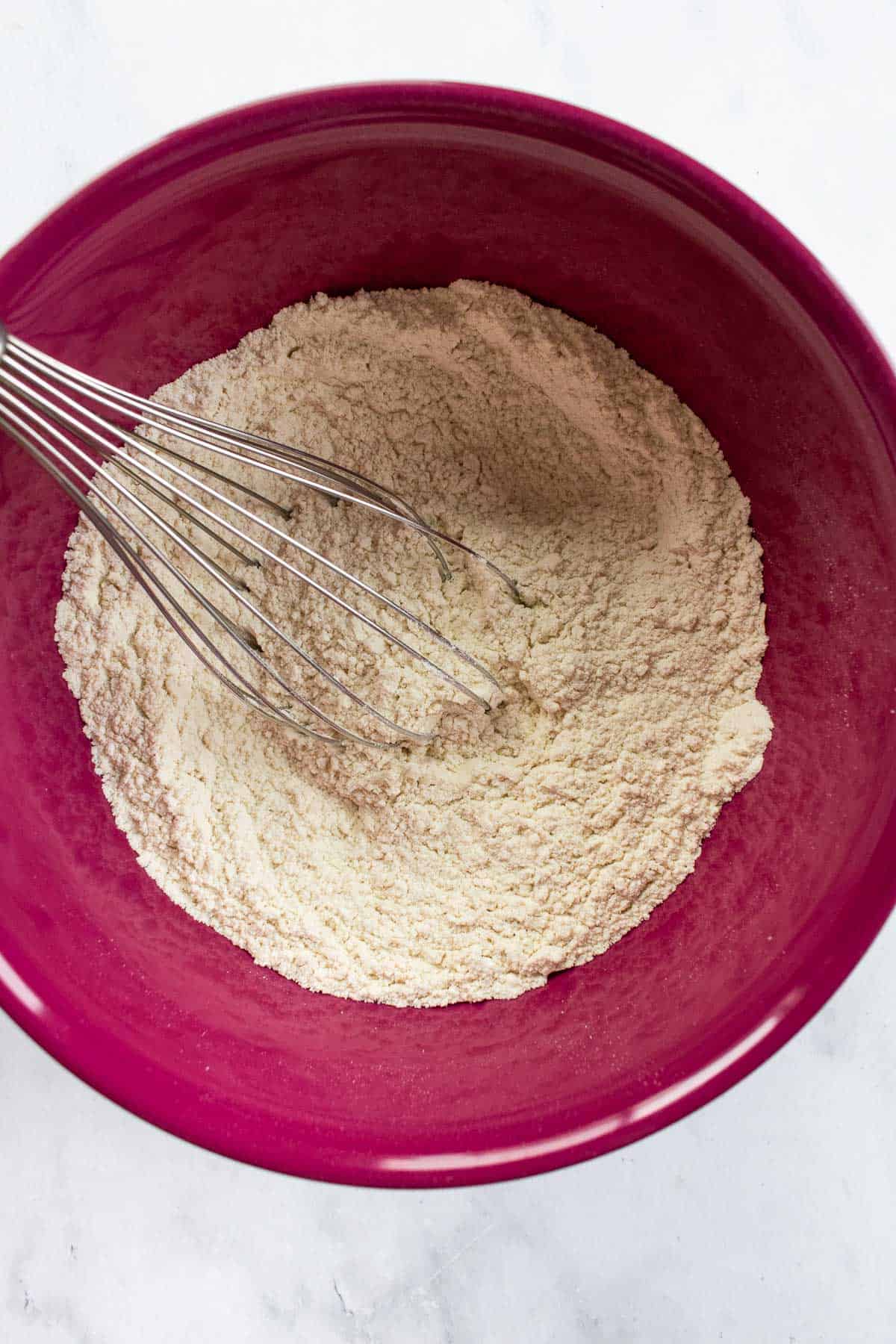 Whisked flour in a magenta bowl with a metal whisk.