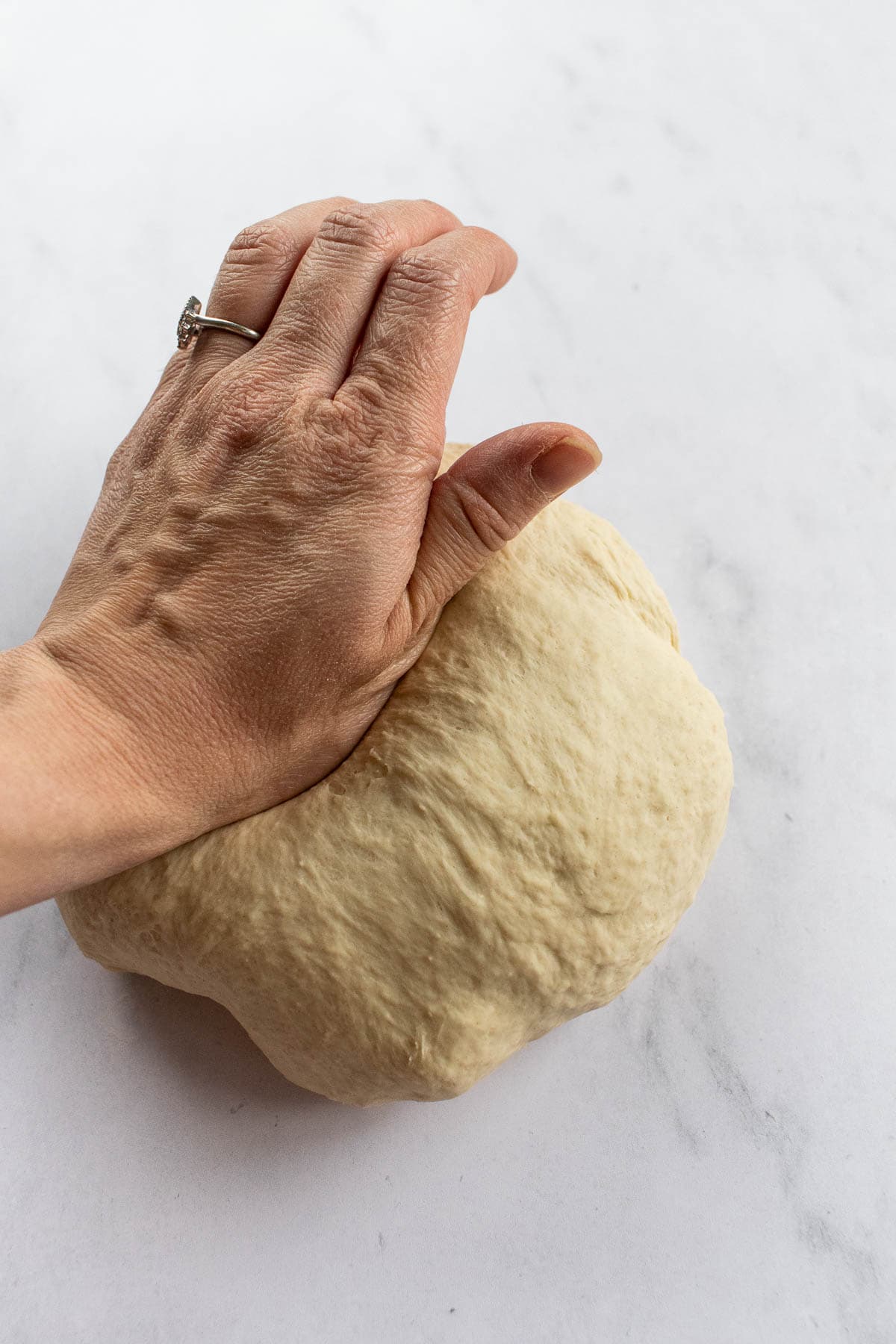 A hand kneading bread dough on a light surface.