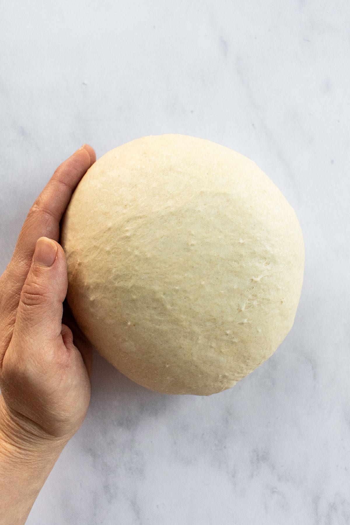 A hand shaping bread dough into a boule.