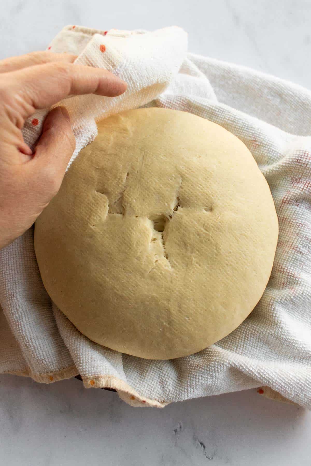 A boule of bread dough with the seam on top in a towel-lined bowl.