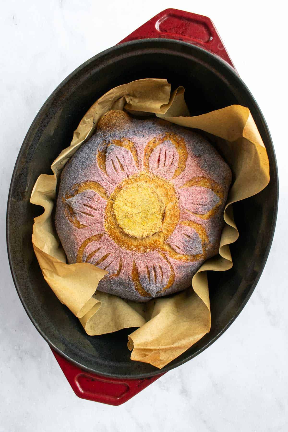 A baked loaf of bread in a Dutch oven scored with flower petals.
