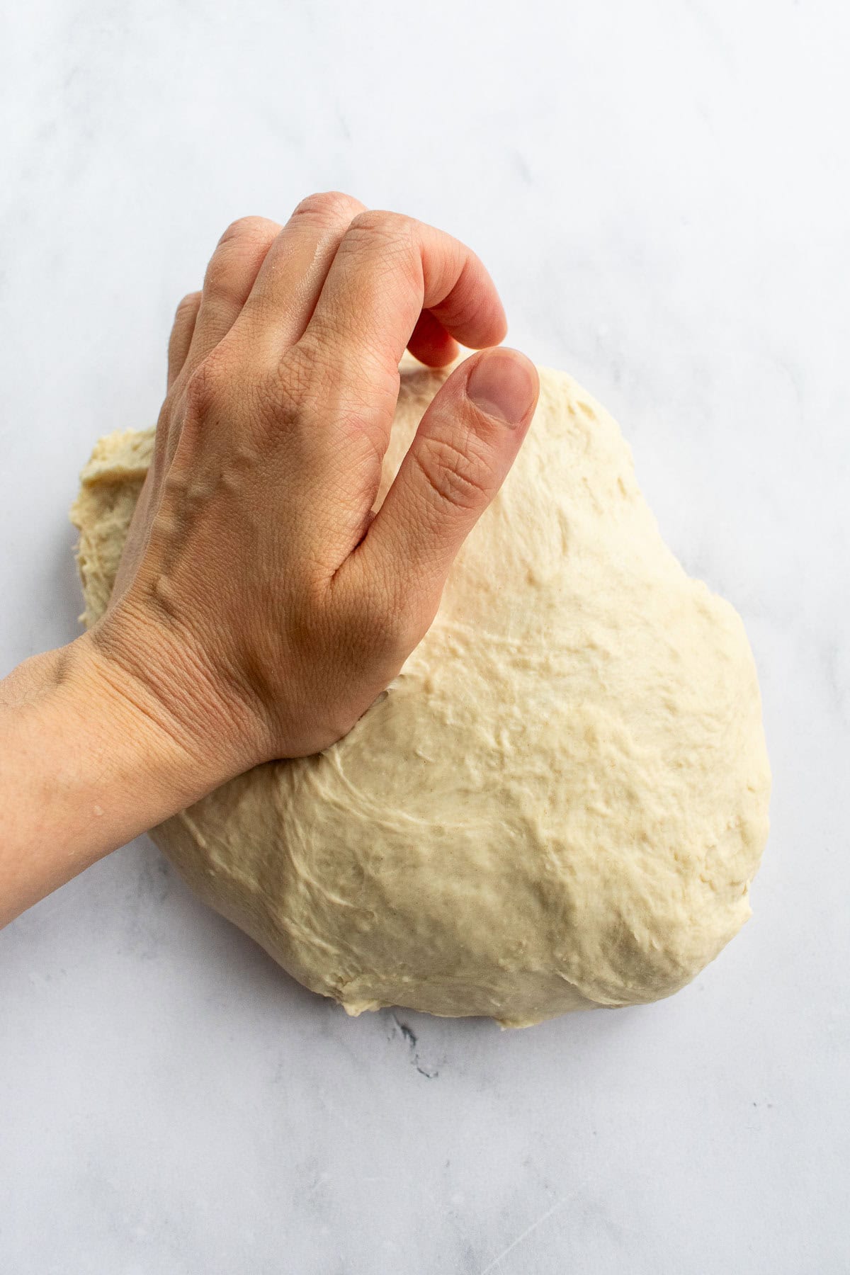 A hand kneading white bread dough on a light surface.