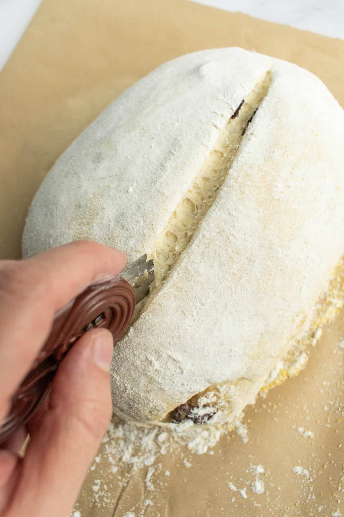 A hand scoring an oval loaf of dough on parchment paper.