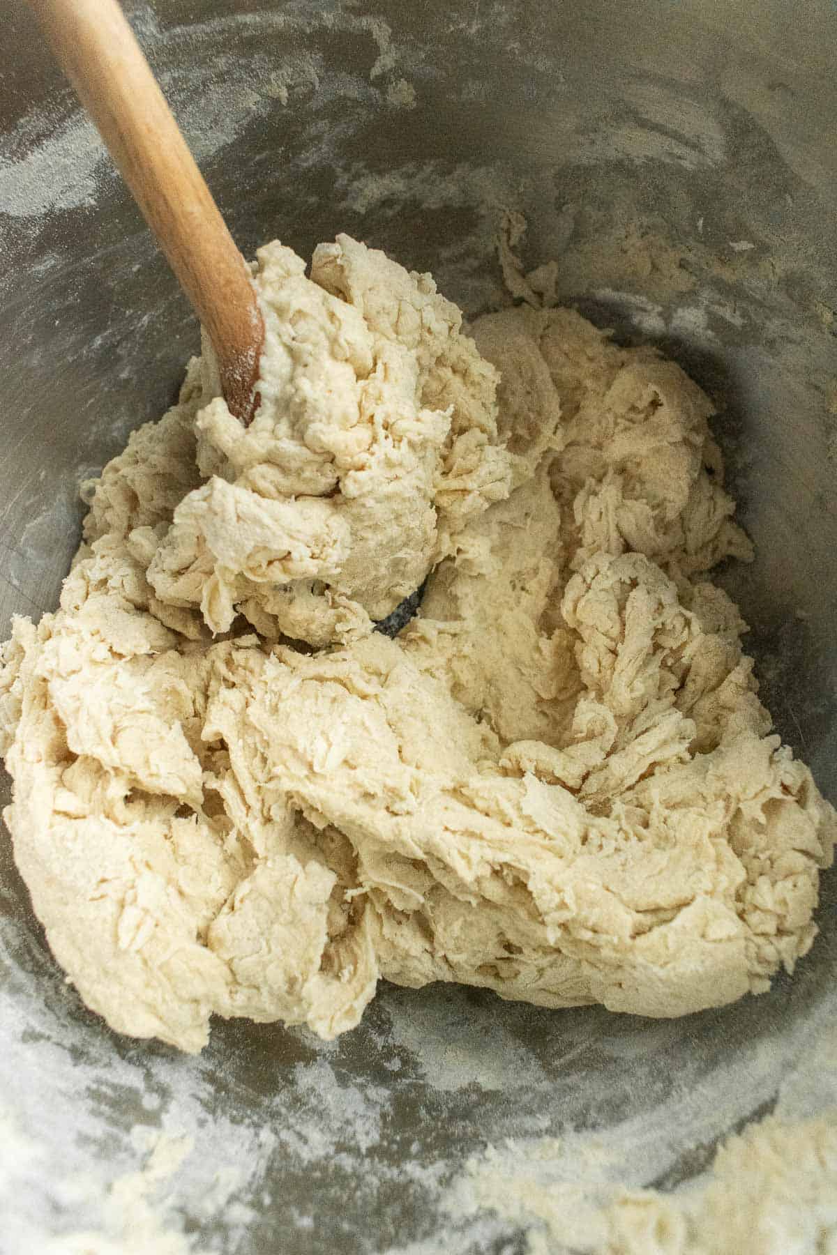 Light beige bread dough in a metal bowl with a wooden spoon.