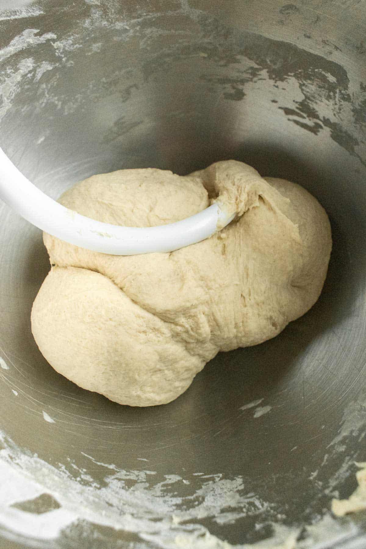 A ball of kneaded dough in a mixing bowl with a dough hook attachment.