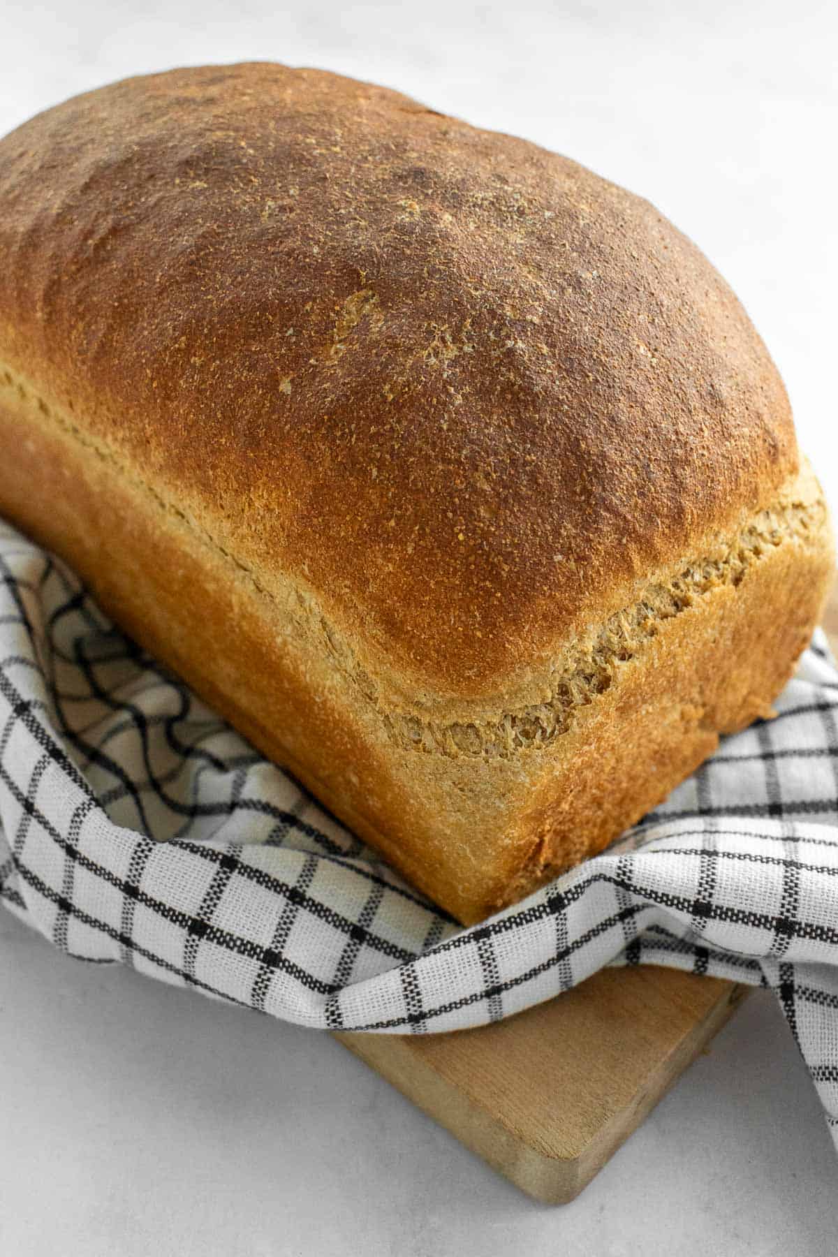A baked loaf of wheat bread on a black and white linen on a wood board.