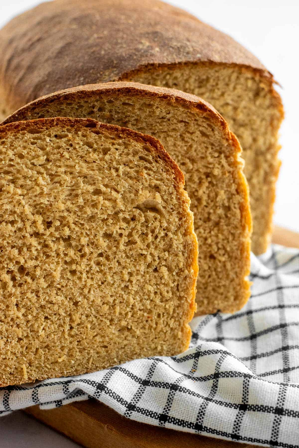 Two slices of wheat bread on a linen leaning against the rest of the loaf.