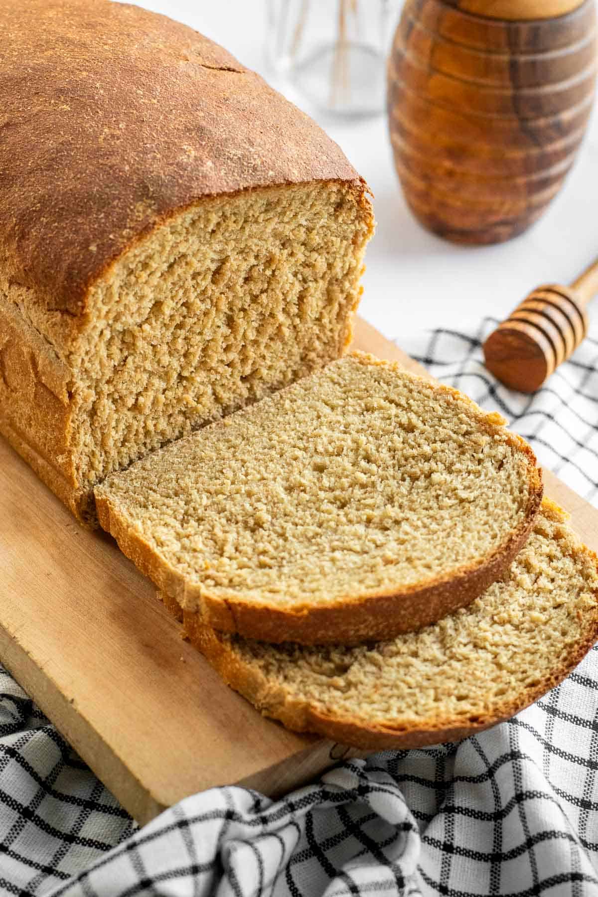 Two slices of sandwich bread on a wood cutting board next to the rest of the loaf.