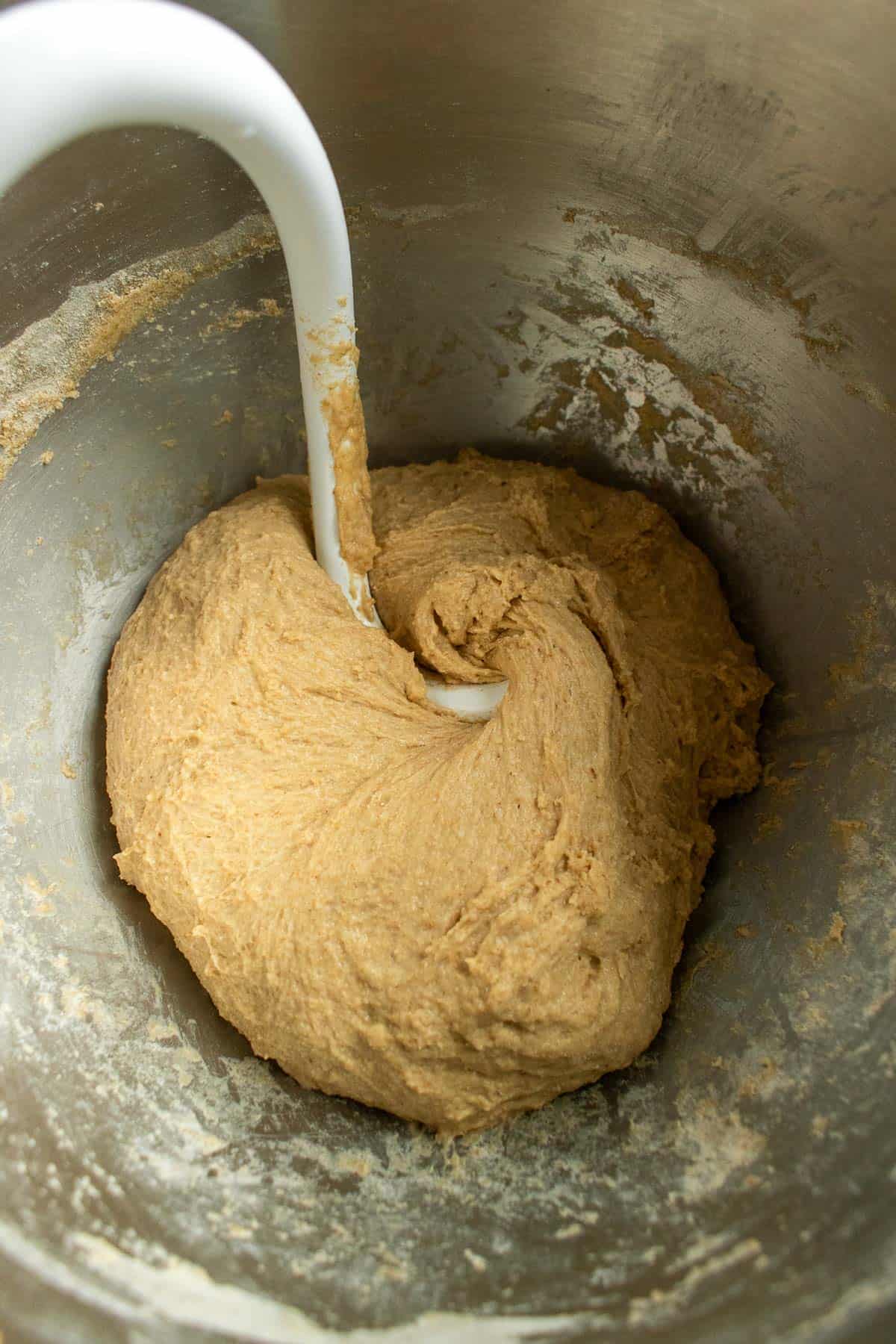 A ball of wheat bread dough in a mixing bowl with a dough hook attachment from a stand mixer.