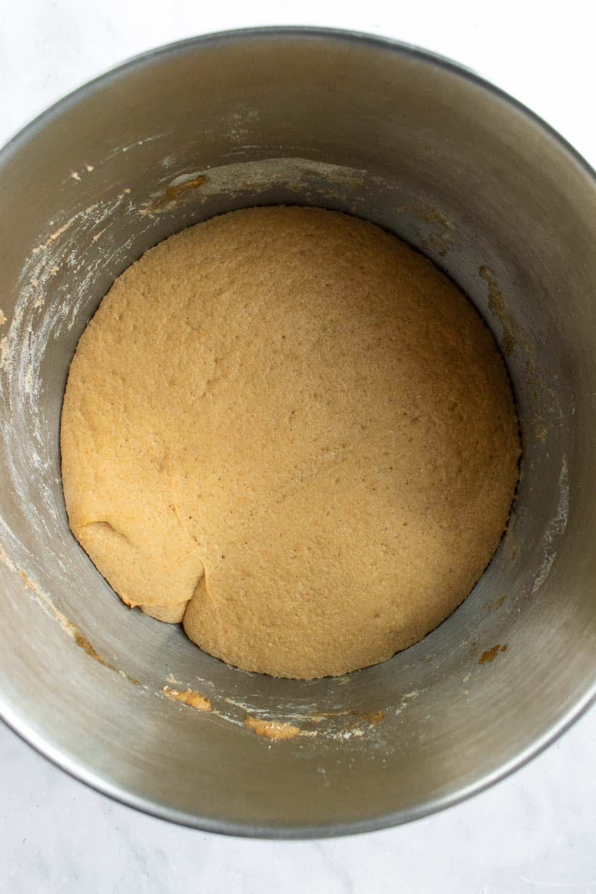 Risen wheat bread dough in a large metal mixing bowl.