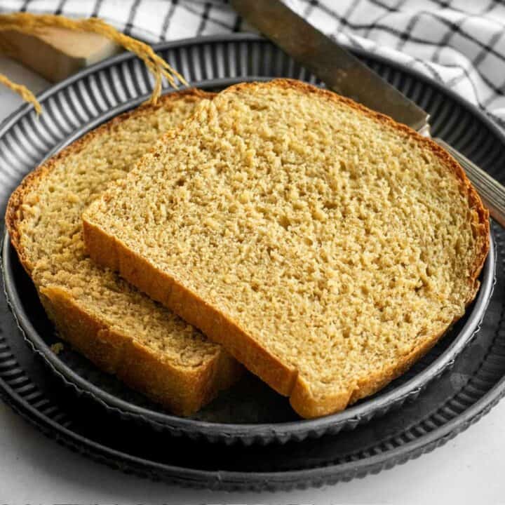 Two slices of wheat sandwich bread on stack metal plates next to a metal butter knife.