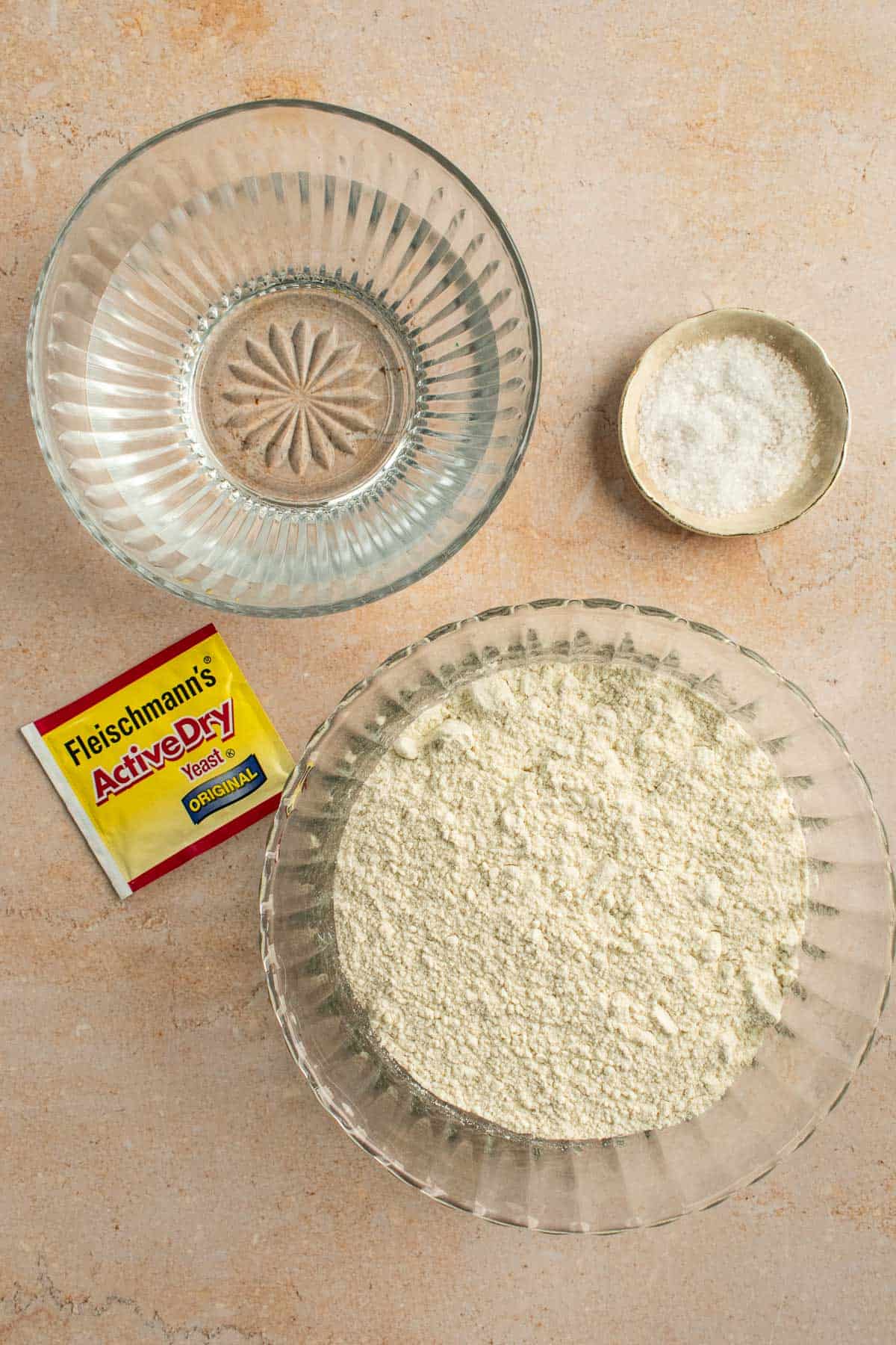 Bowls of water, flour, and salt next to a packet of active dry yeast.