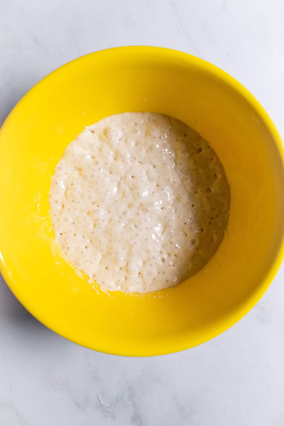 A bubbly, risen poolish in a yellow mixing bowl.