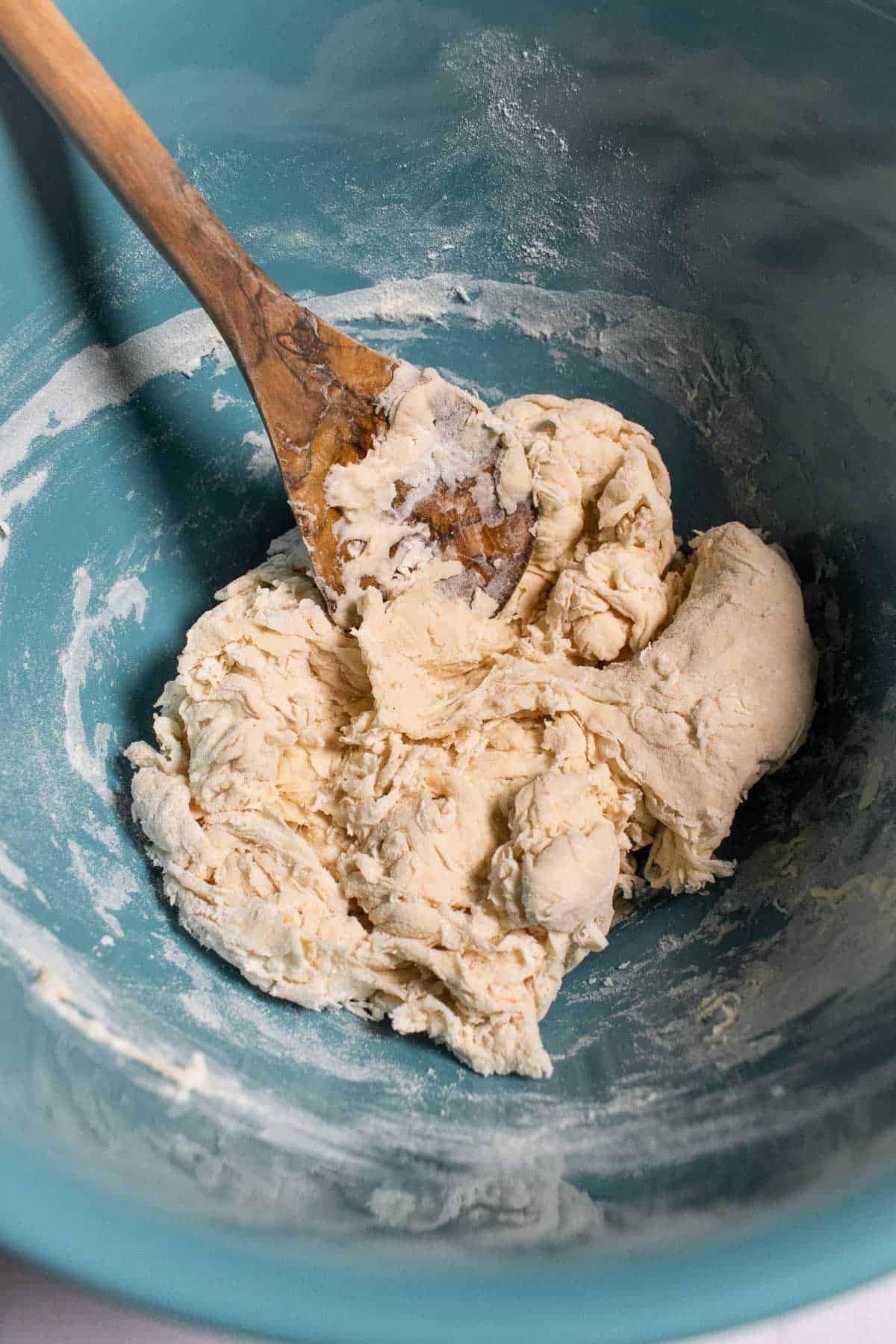 A shaggy, dry dough in a blue mixing bowl with a wooden spoon.