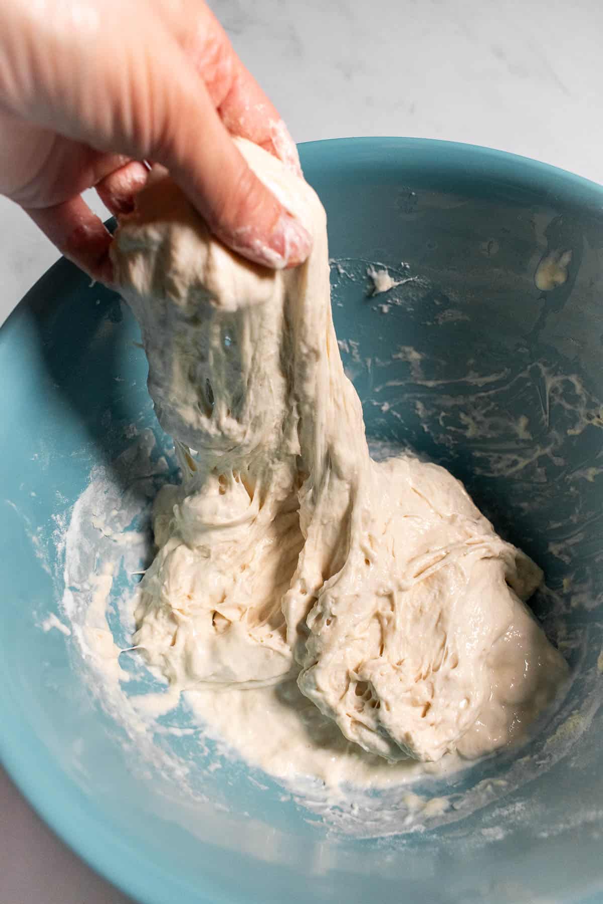 A hand stretching a handful of bread dough out of a bowl.
