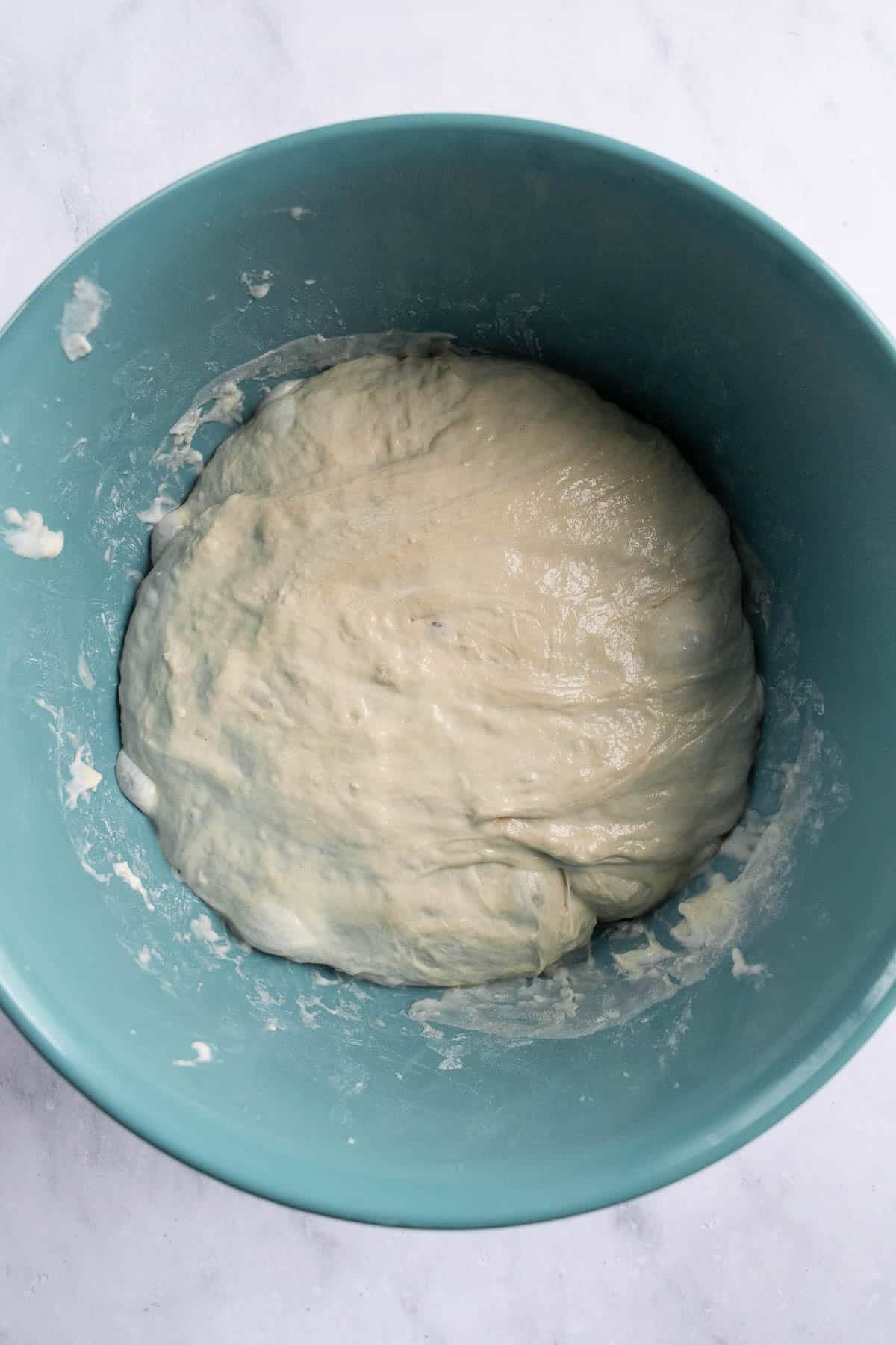 Risen, slightly bubbly white bread dough in a blue bowl on a light surface.