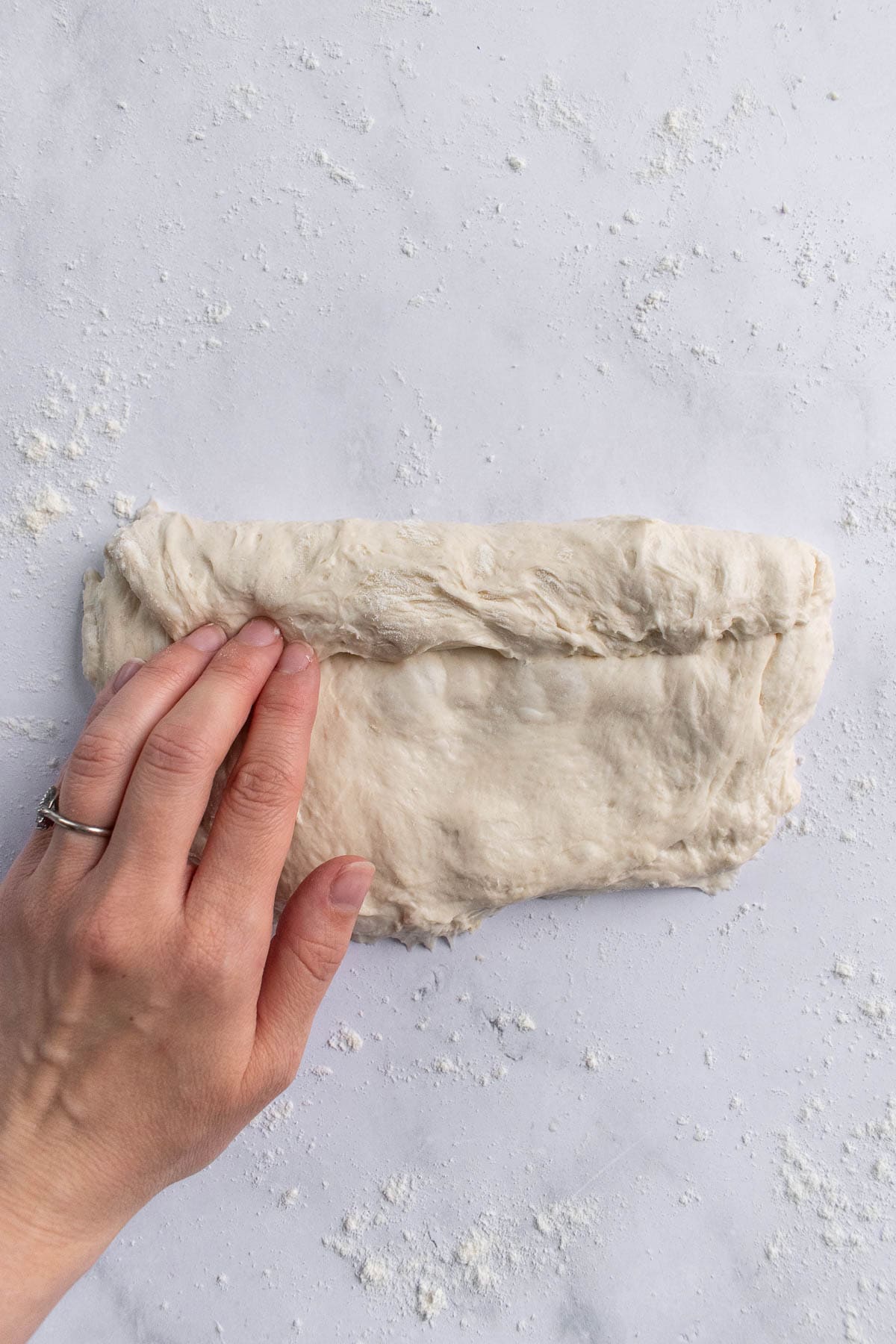 A hand folding and pressing a rectangle of dough in thirds on a counter.