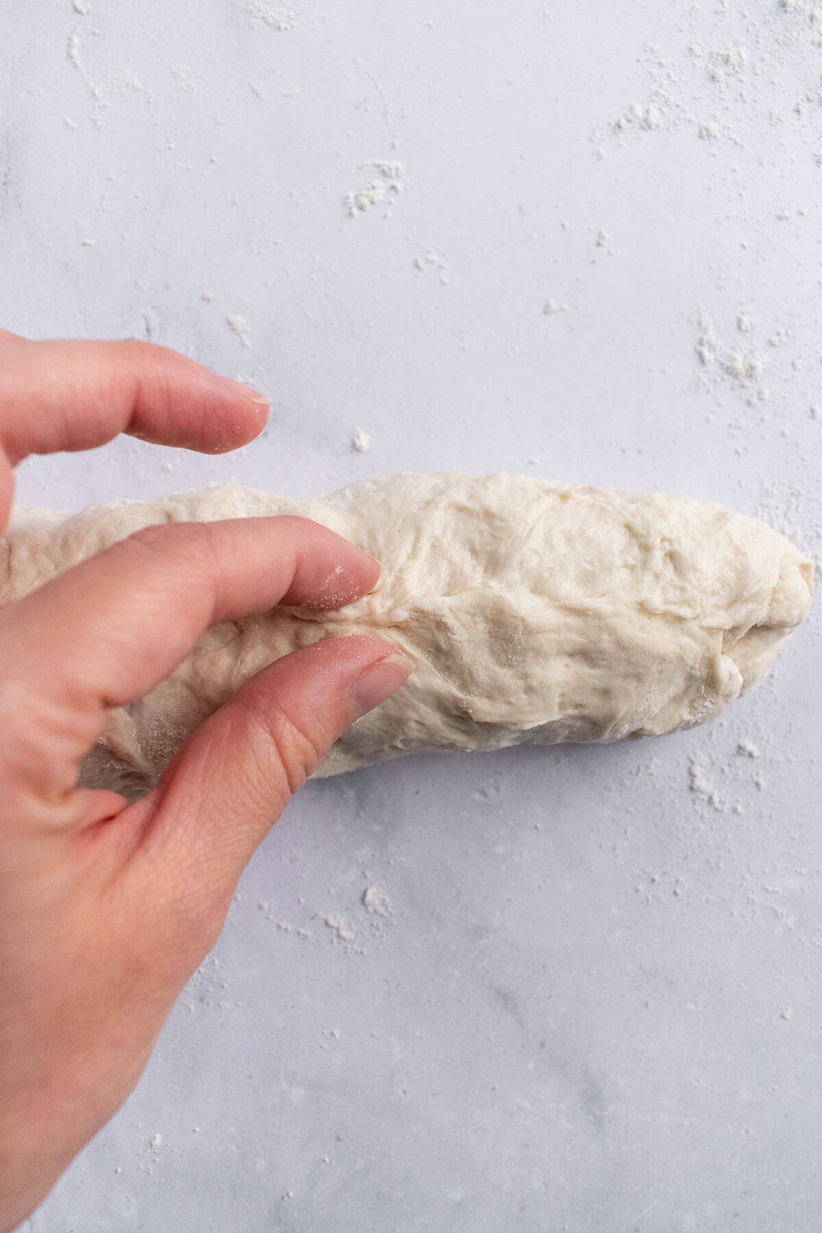 A hand pinching the seam on an unbaked baguette on a light surface.