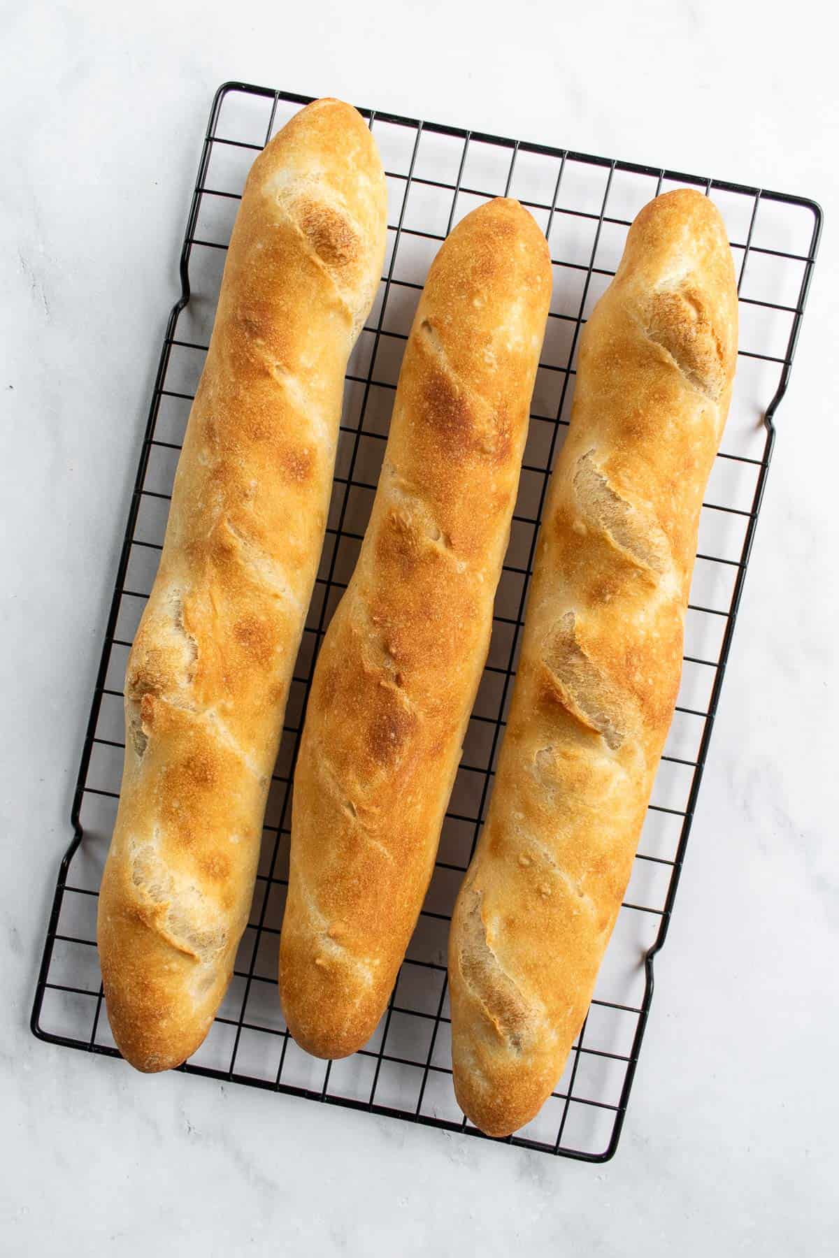 Three golden baked loaves of baguettes on a wire cooling rack.