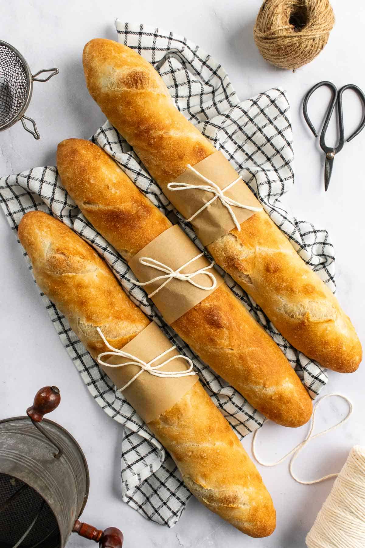 Three long baguettes on a kitchen linen wrapped in small pieces of brown paper and tied with string.