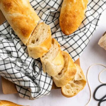 Two whole baguettes next to a sliced baguette on a black and white linen.