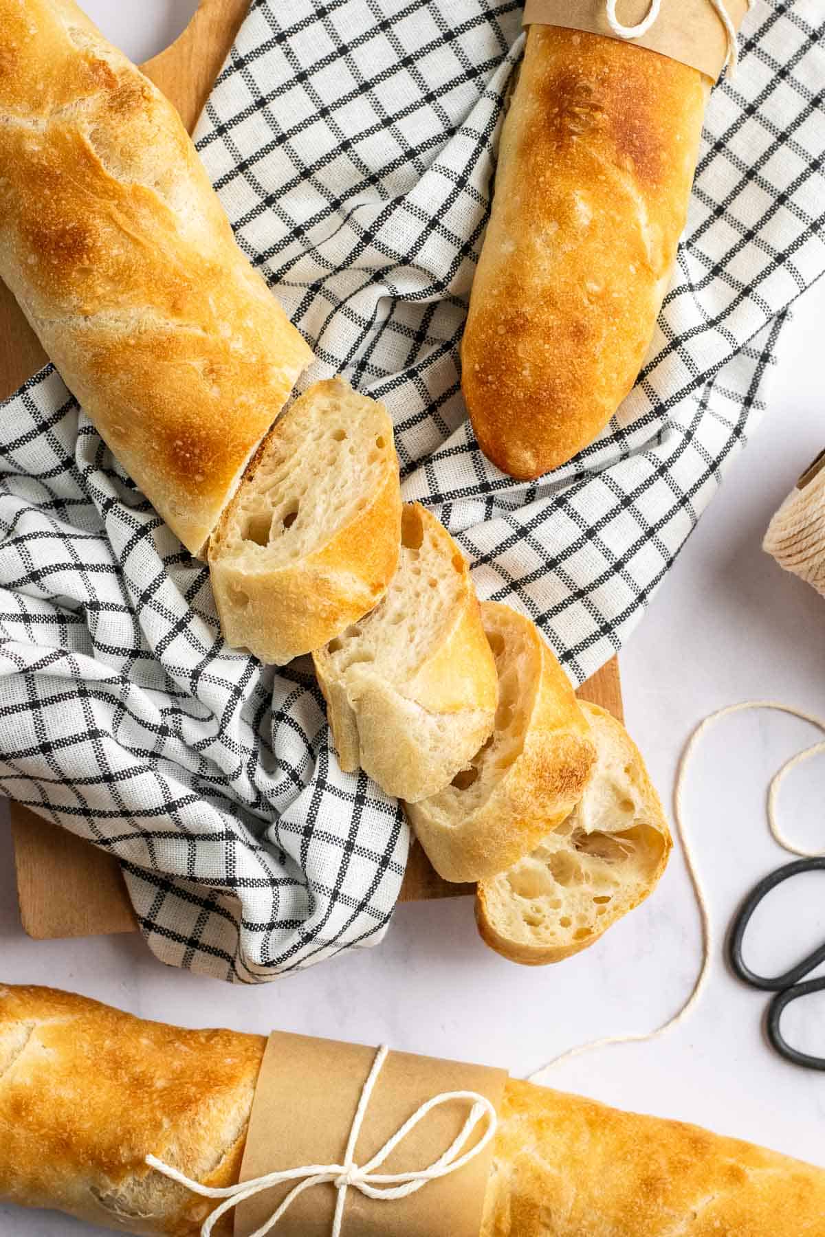Two whole baguettes next to a sliced baguette on a black and white linen. 