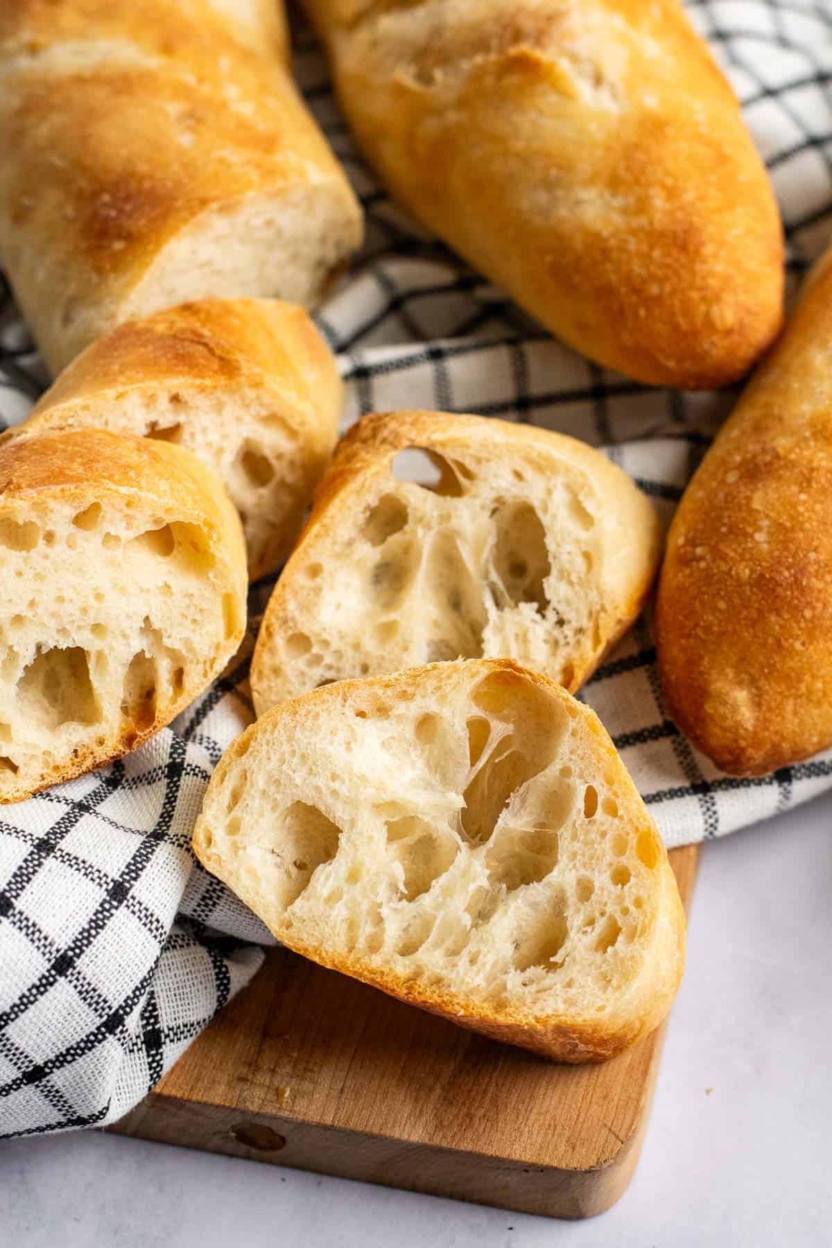 Slices of an open, airy baguette on a wood board covered with a black and white linen.