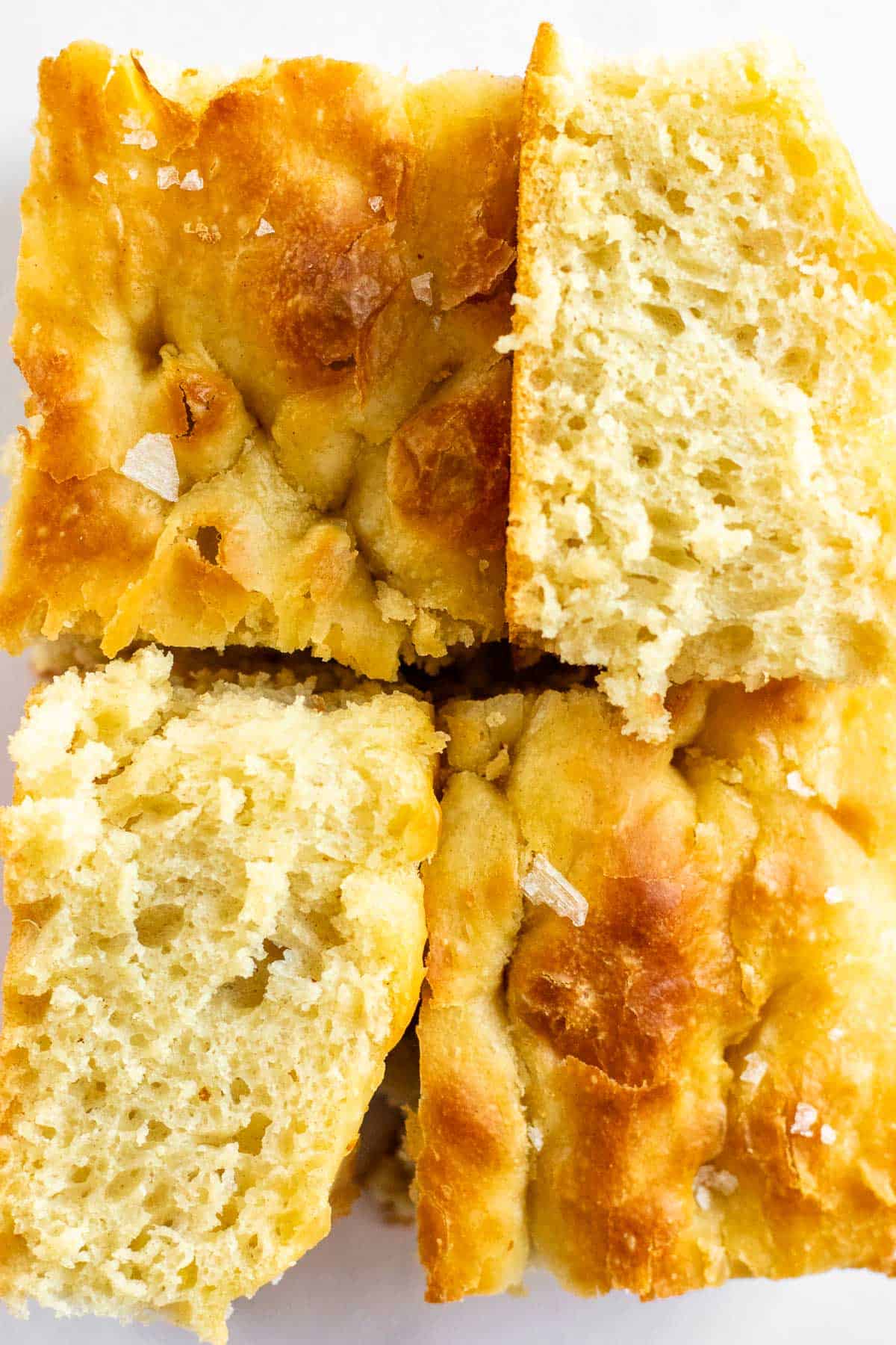 Four squares of focaccia bread, with two of them on their sides, all topped with flaky salt.