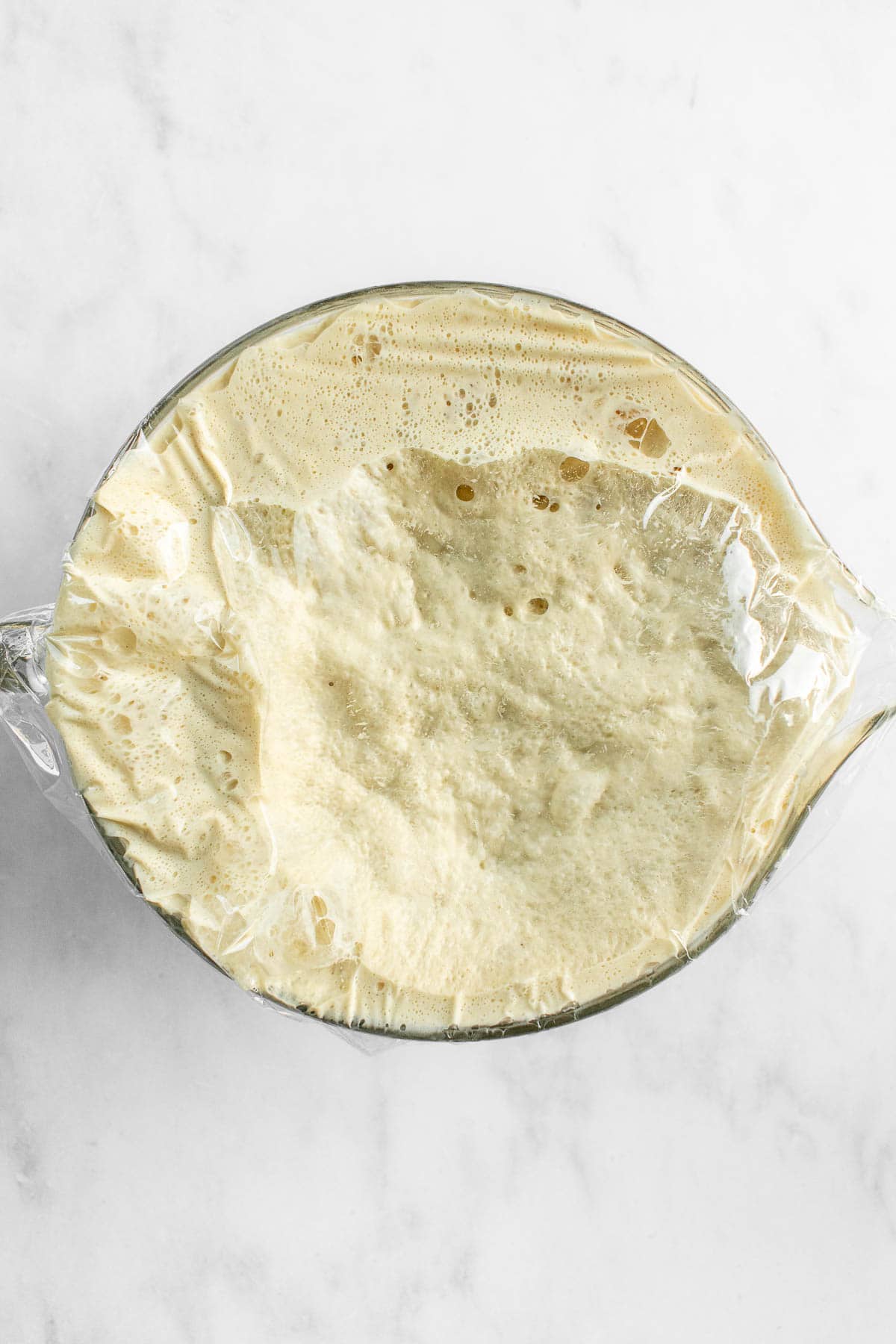 A bowl completely filled with bubbly, risen bread dough on a light surface.