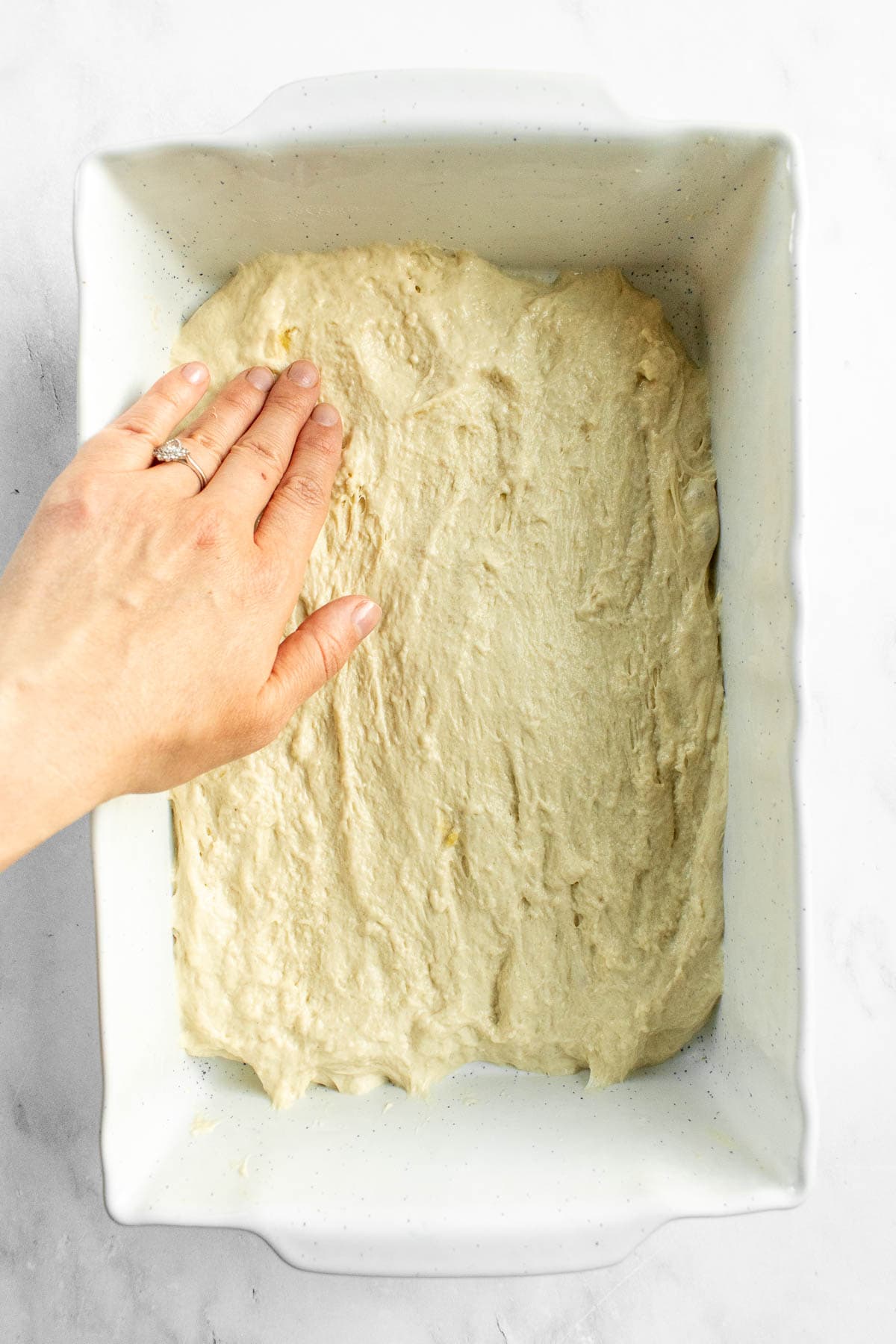 A hand pressing bread dough to fill the bottom of a large baking dish.