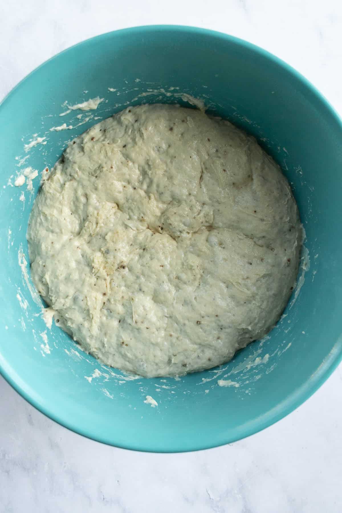 A blue mixing bowl filled with risen bread dough with ground black pepper in it.